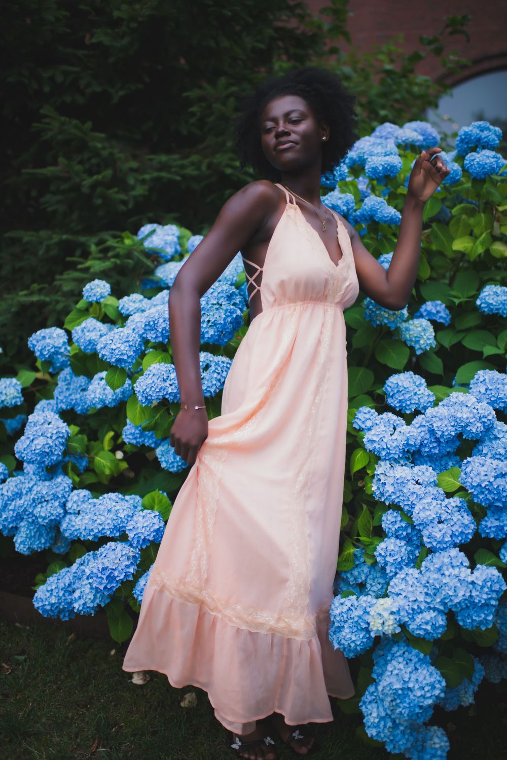 Elegant summer fashion with peach dress against vibrant blue hydrangea garden backdrop.