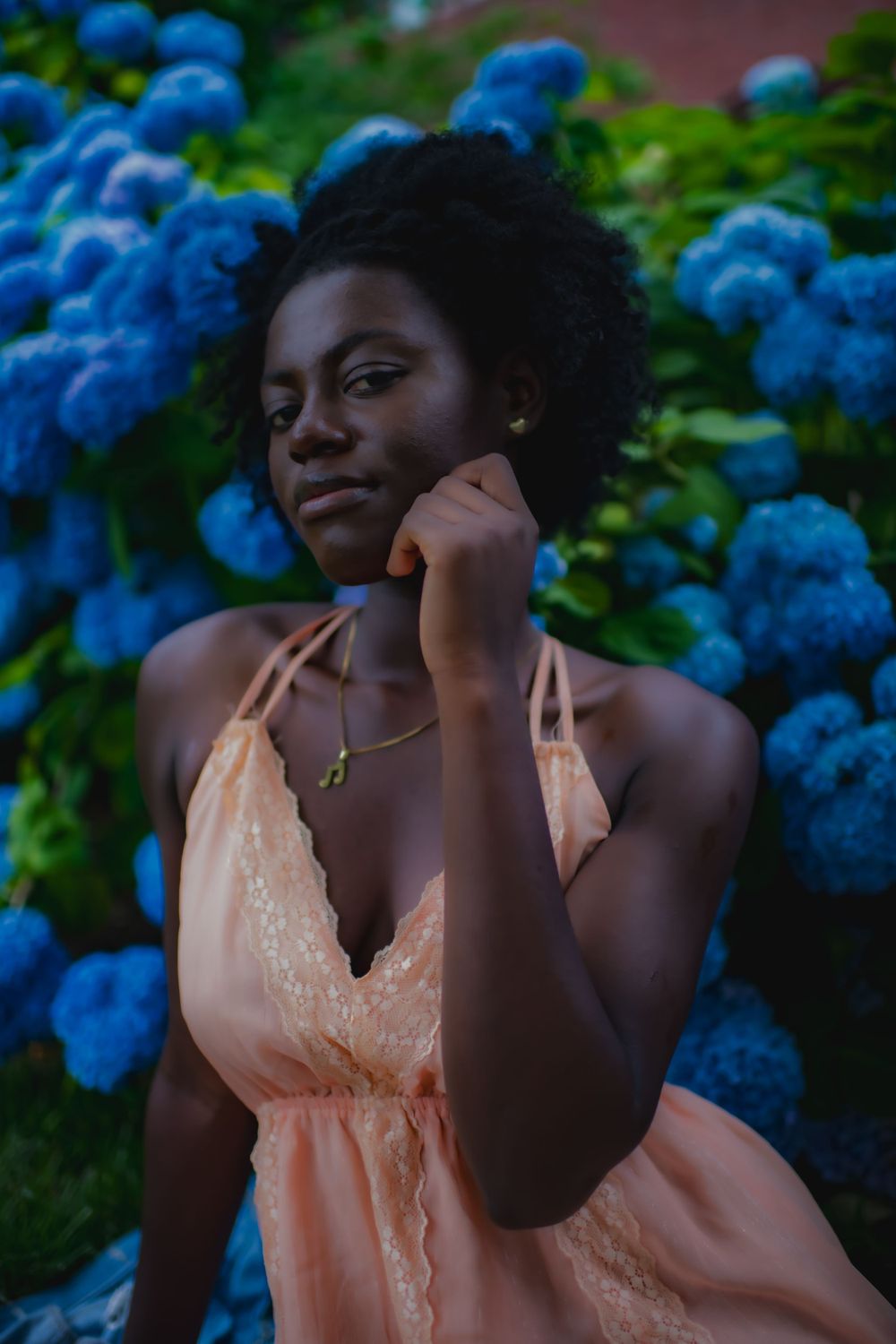 Portrait against vibrant blue hydrangeas wearing a delicate peach-colored lace dress.
