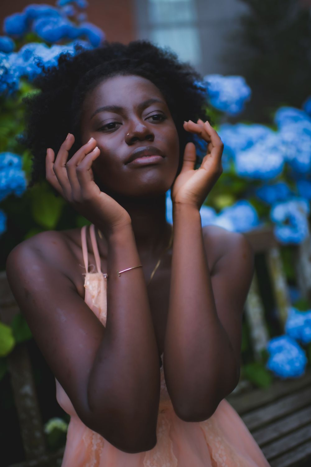 Portrait against vibrant blue hydrangeas with gentle hands framing face.