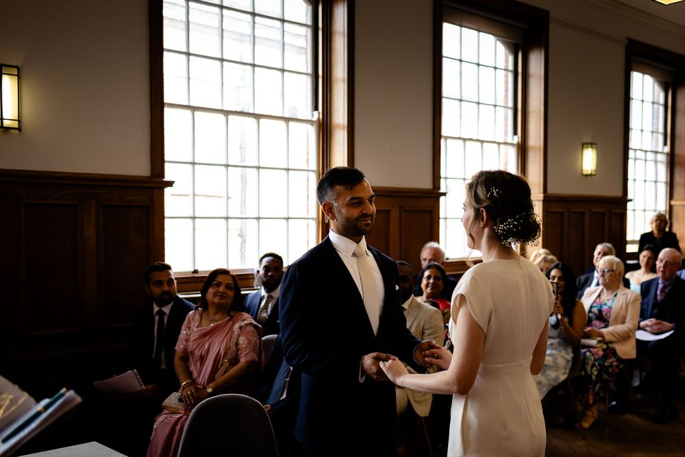 Wedding ceremony in progress inside historic building with large windows and wooden interior.