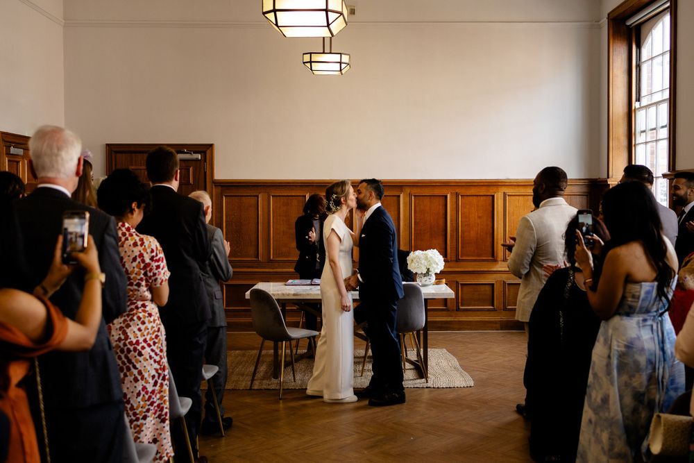 Wedding ceremony taking place in wood-paneled room with guests watching.