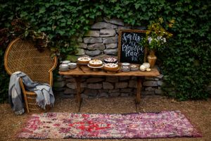 Rustic dessert display with chalkboard sign against ivy-covered stone wall and vintage wicker chair.