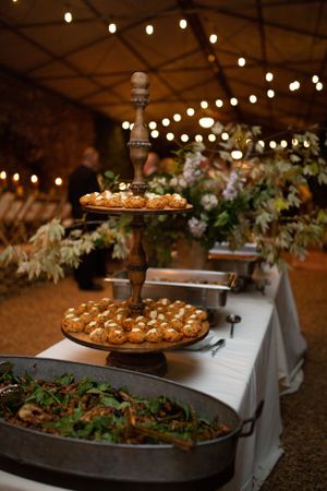 Buffet table with tiered dessert stand and string lights at rustic wedding reception.