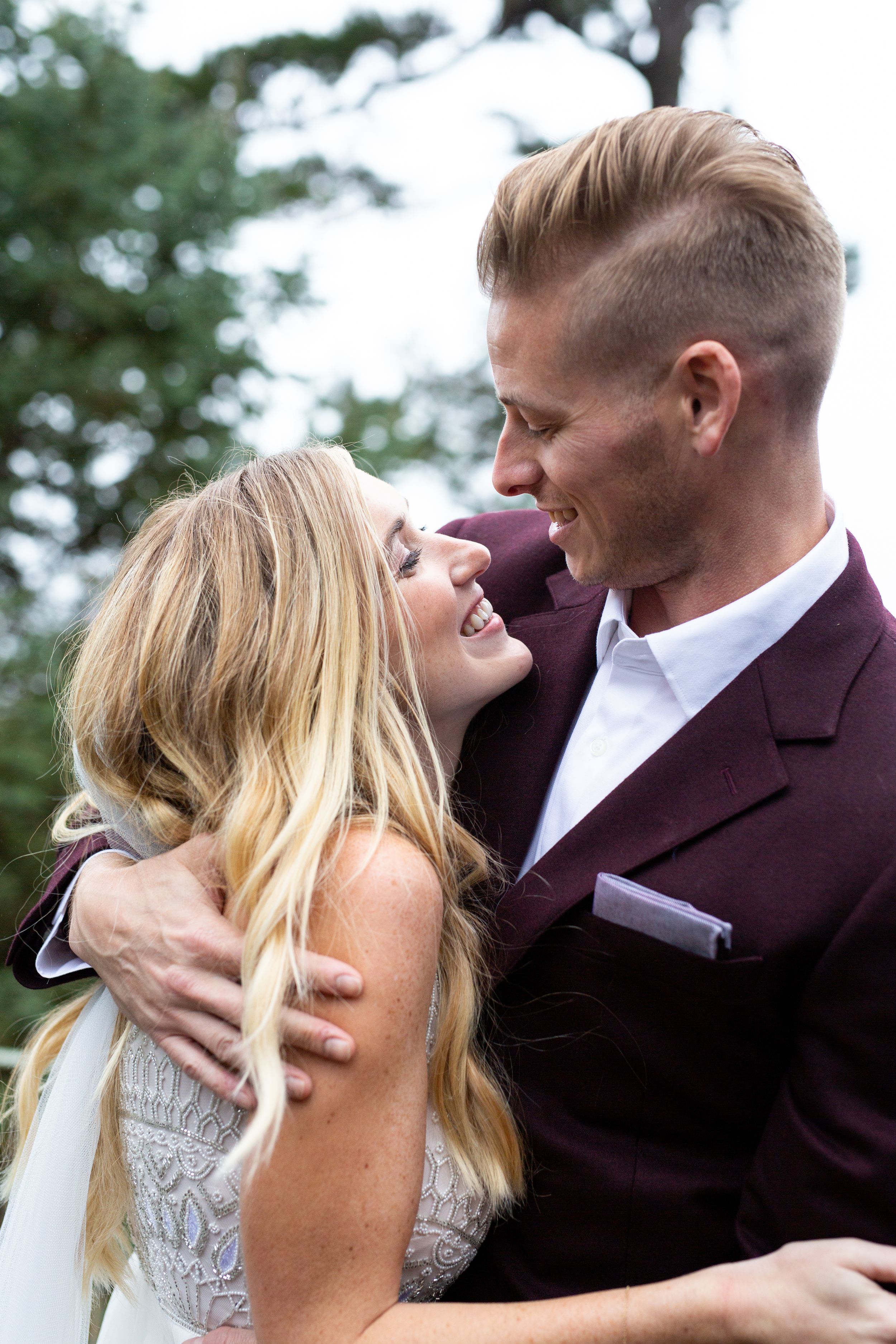A joyful moment shared between a couple in wedding attire against a forest backdrop.