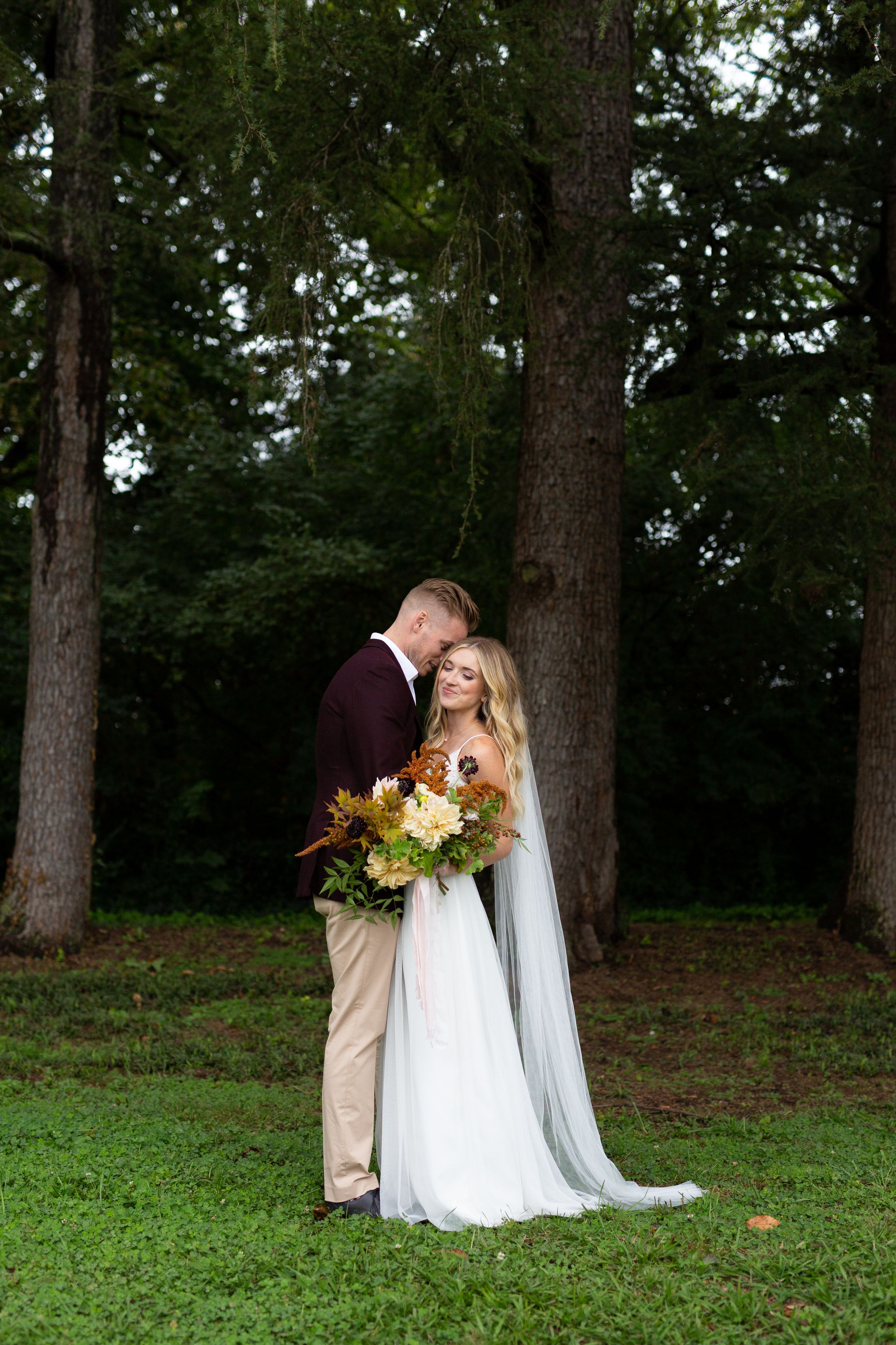 A romantic outdoor wedding portrait with pine trees in the background and a colorful bouquet.