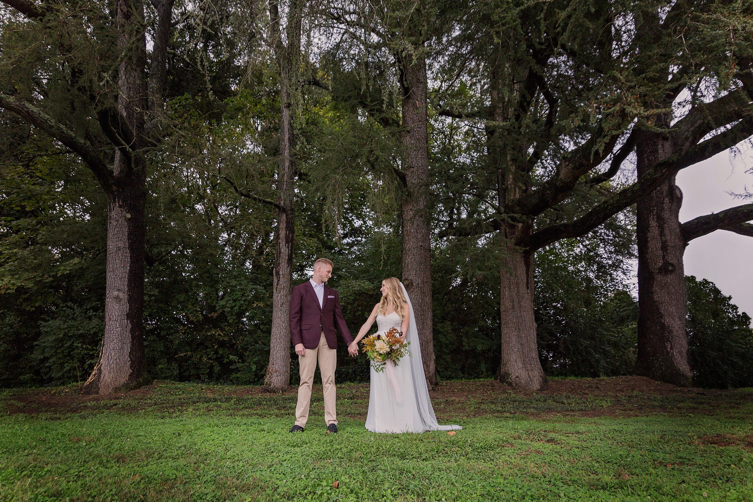Wedding couple standing among tall trees in outdoor forest setting.