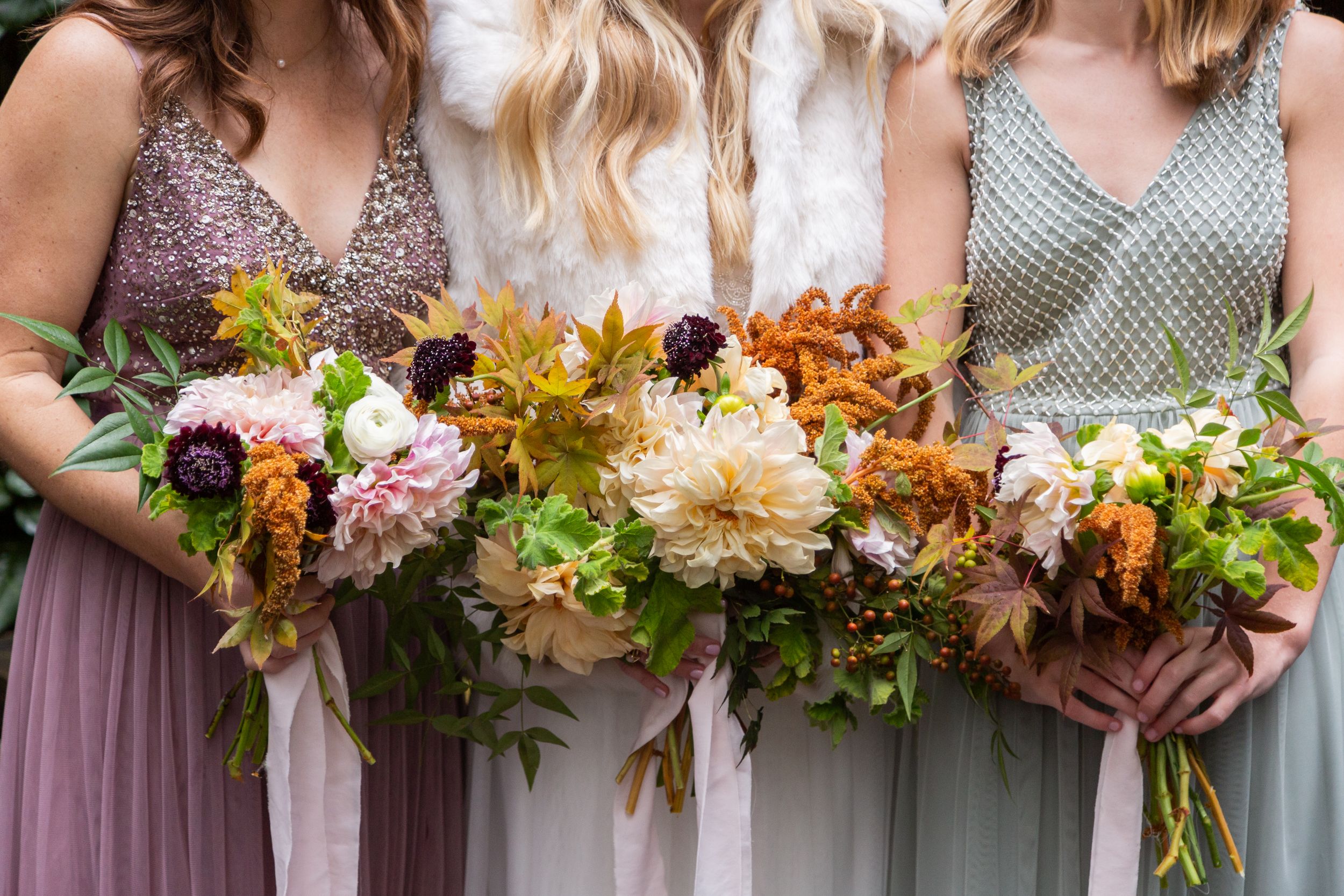 Row of autumn-colored wedding bouquets held against pastel bridesmaid dresses.