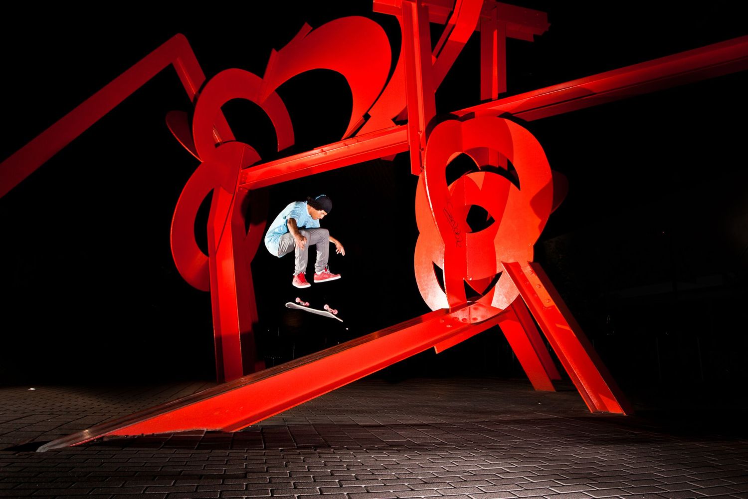 Skateboarder performs trick against dramatic red light art installation at night.