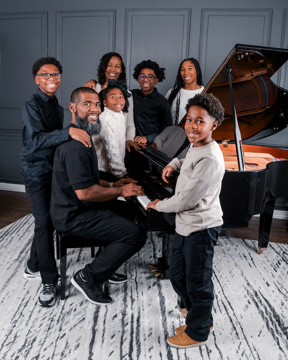 Family portrait session with coordinated black and white outfits around a grand piano.