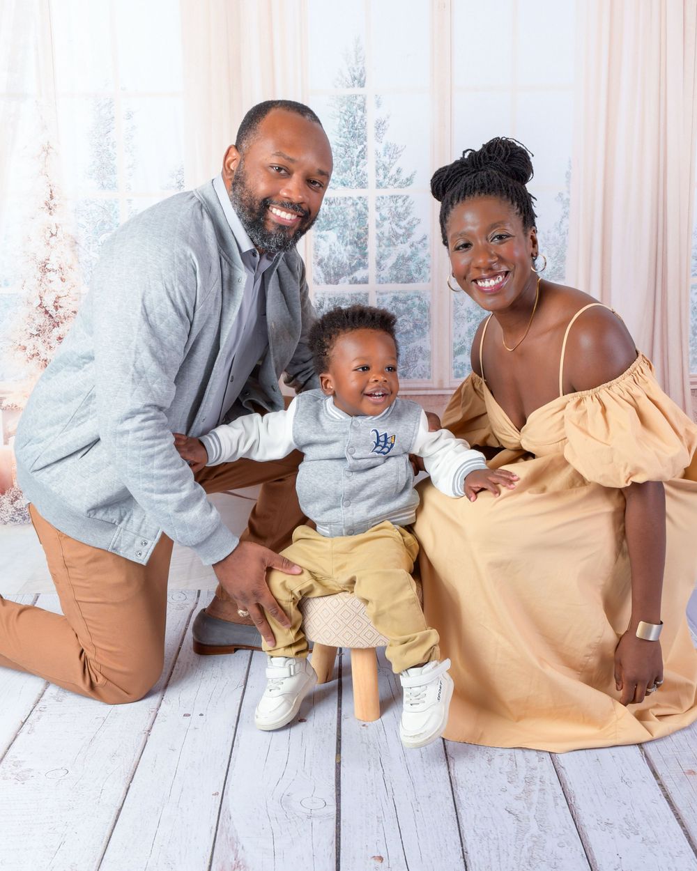 Family of three posing together on white wooden floor with holiday decor in background.