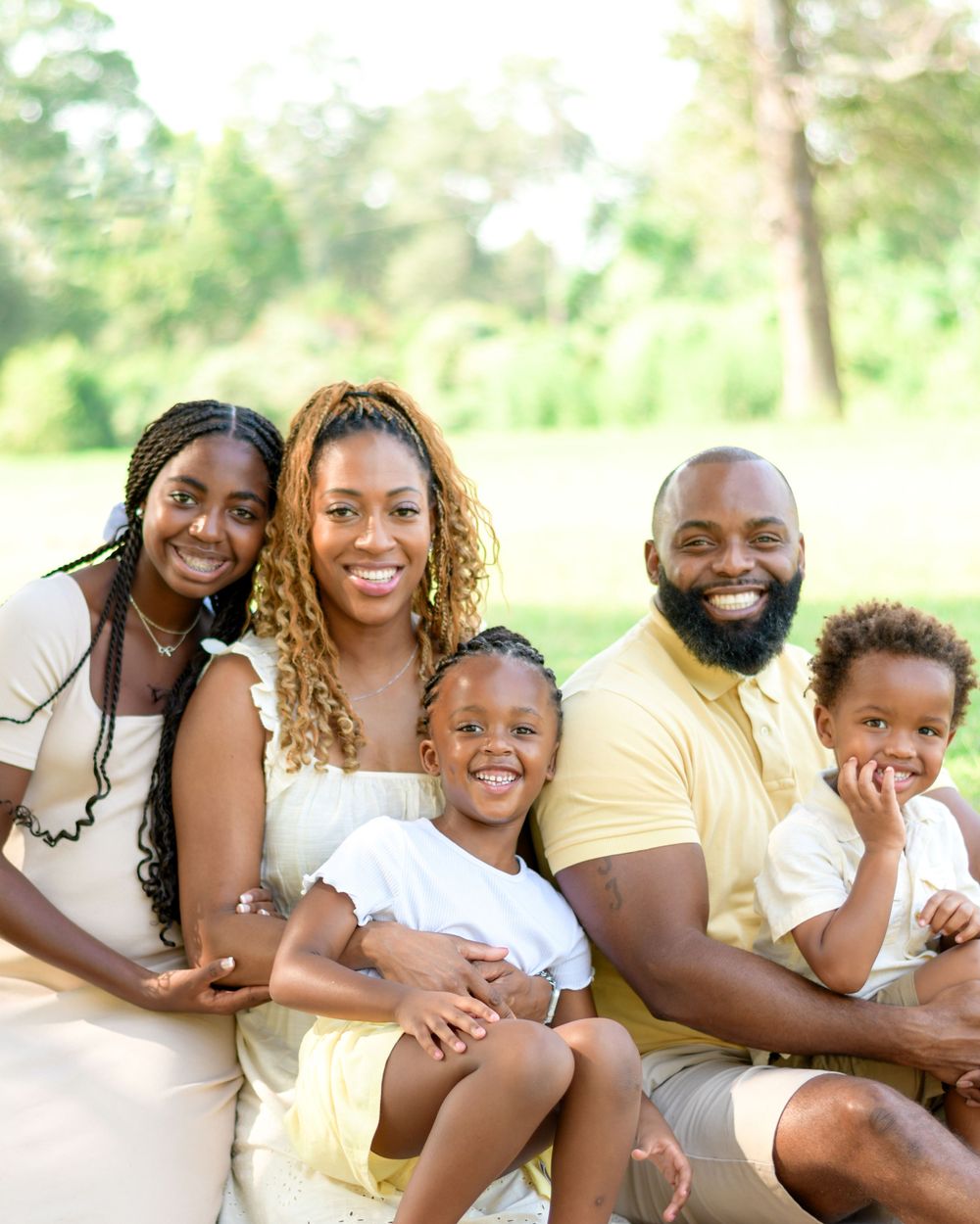 Joyful family of five sitting together outdoors in white and yellow outfits during a sunny day.