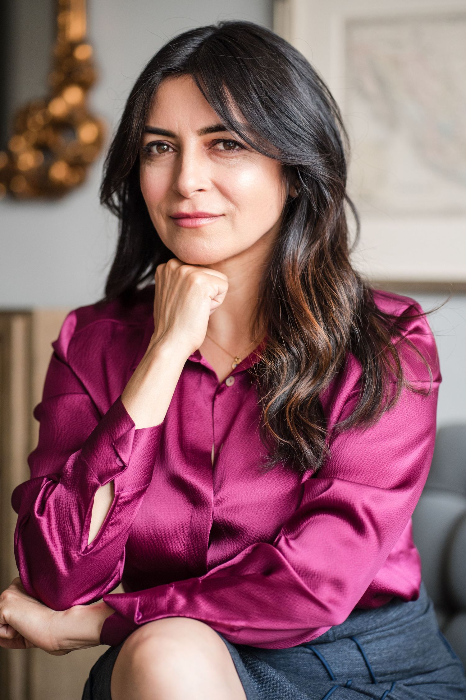 Woman in magenta silk blouse sits thoughtfully with hand near chin.