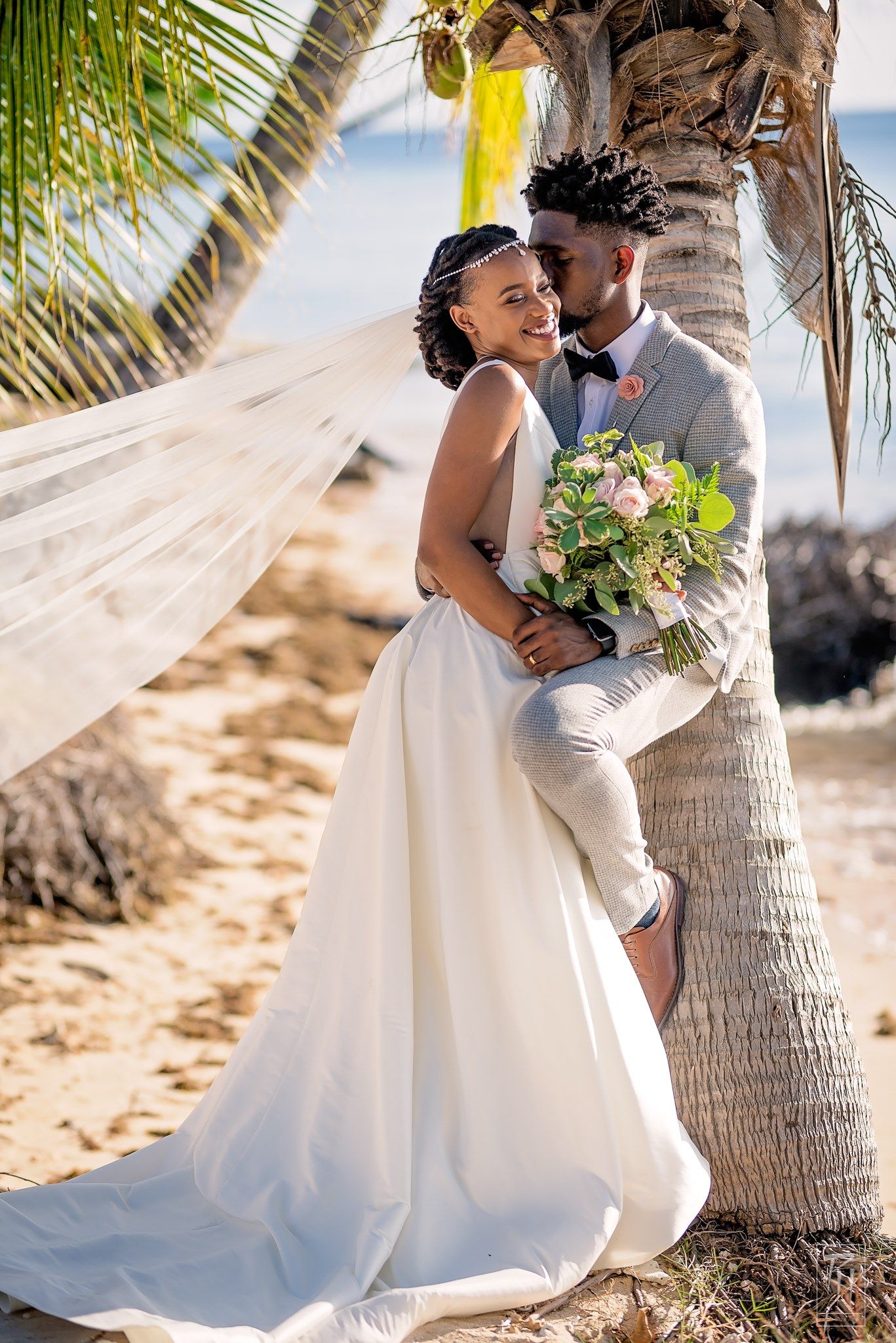 Beach wedding portrait with couple embracing by palm tree with flowing white dress.