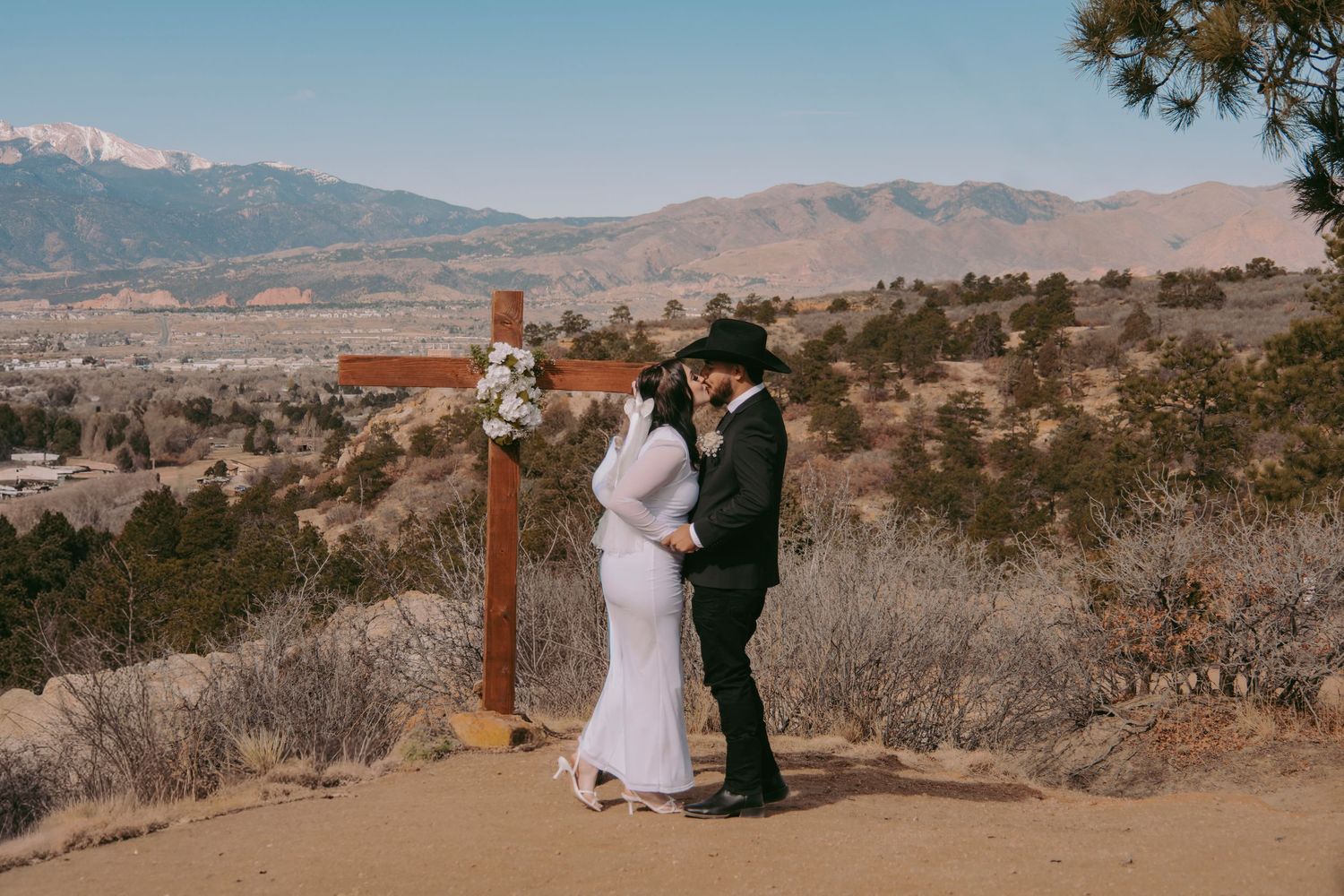 Bride and groom share a kiss at rustic cross altar with stunning mountain backdrop at outdoor wedding.