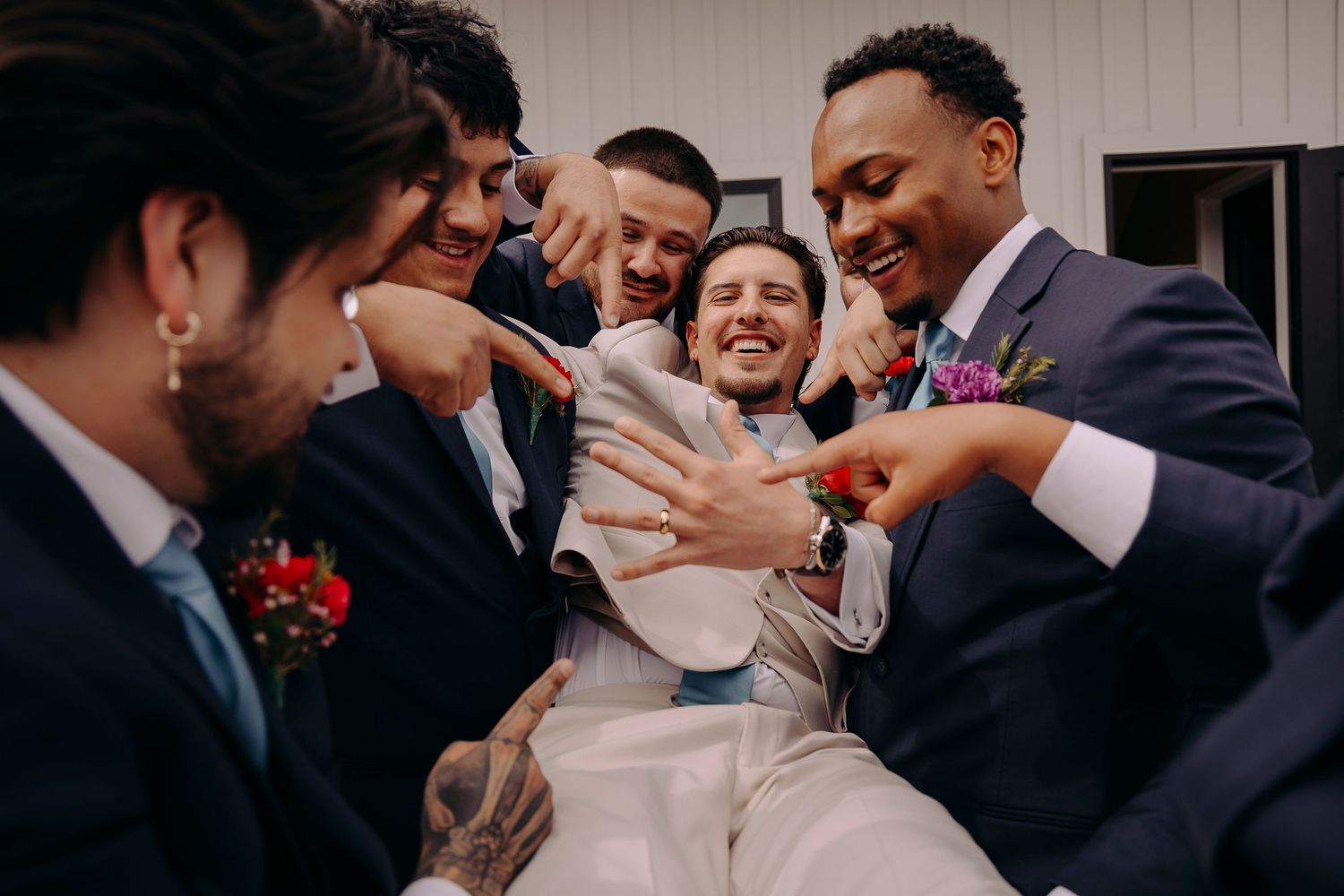 Groomsmen laughing and celebrating with the groom at a wedding reception outdoors.