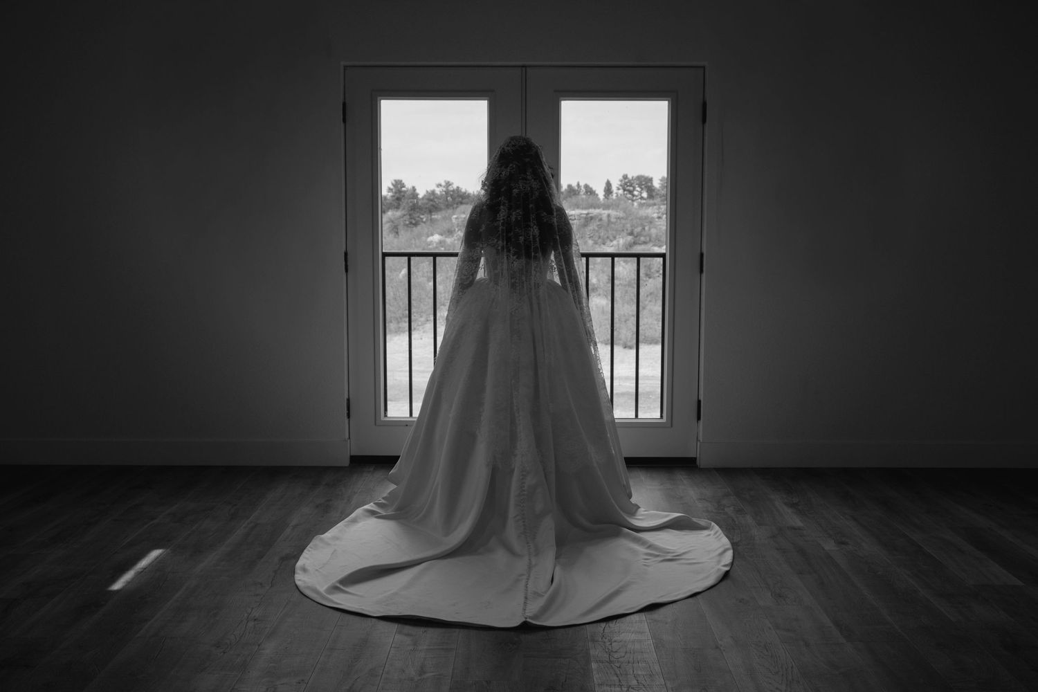 Bride in a white gown with long train standing before French doors in black and white.
