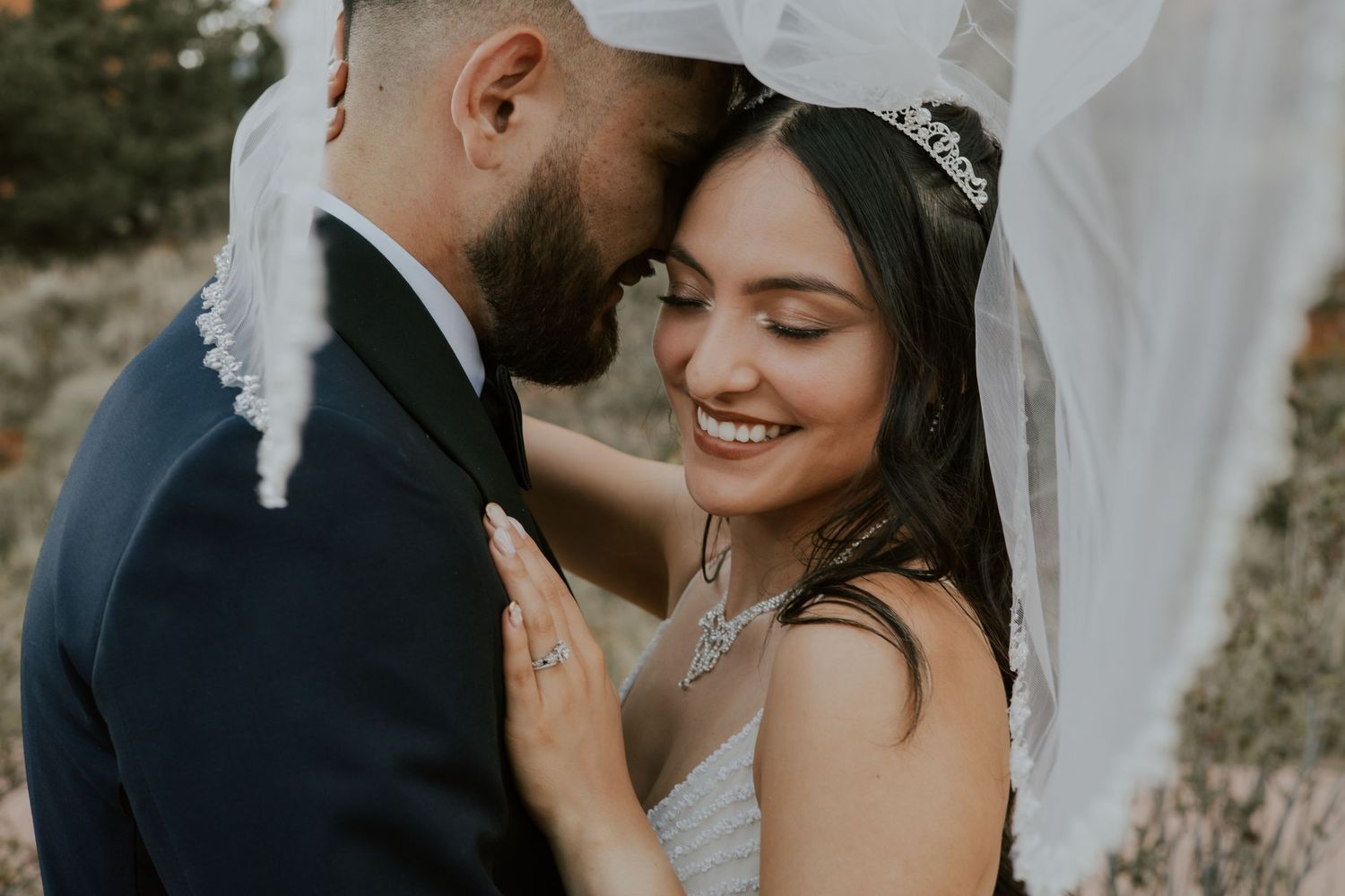 Bride and groom sharing intimate moment under wedding veil, smiling together in close portrait.