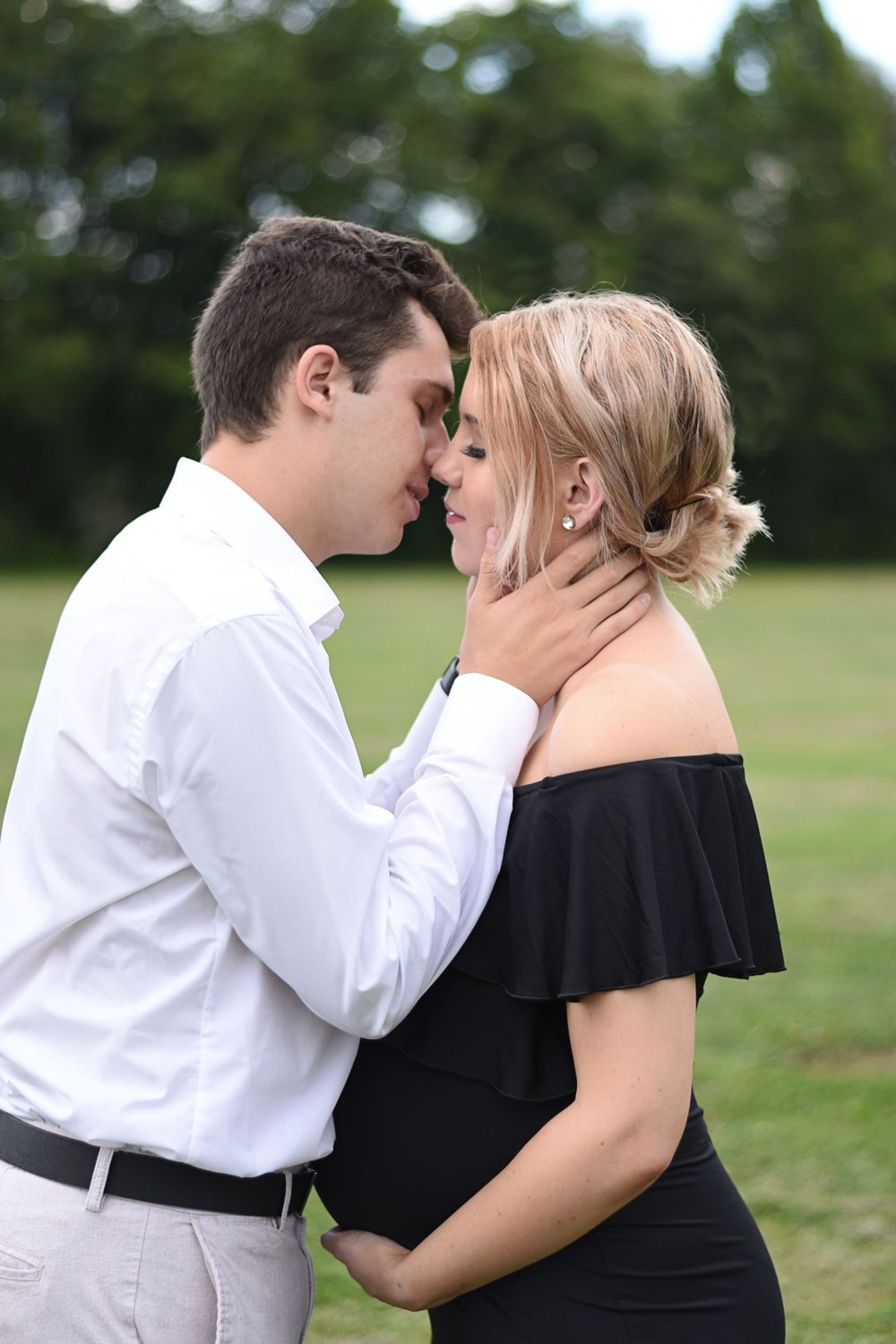 Romantic maternity photos of couple embracing in an outdoor field setting.