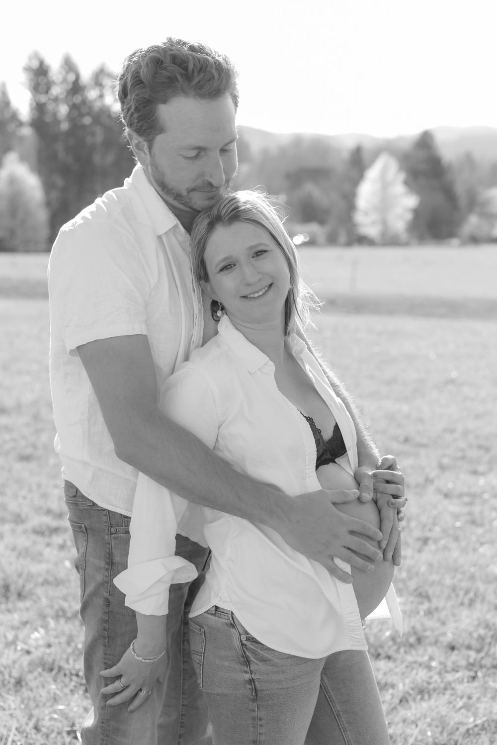 A casual black and white portrait in a sunny meadow with trees in background.