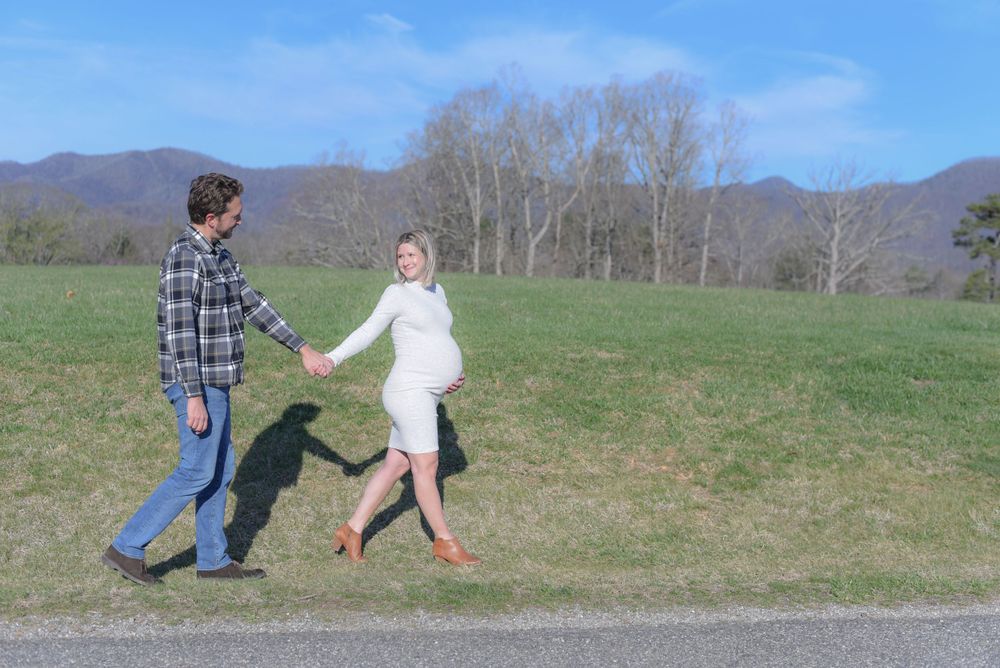 A couple poses playfully in a grassy field with mountains in the background.