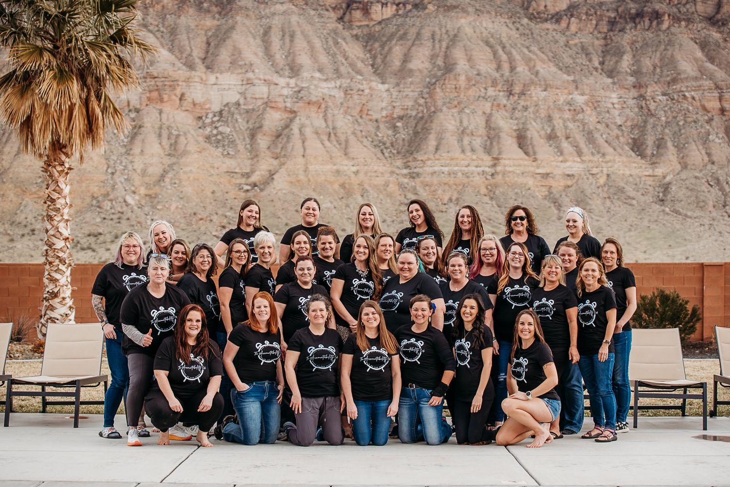 Large group in black shirts poses together outdoors against desert mountain backdrop.