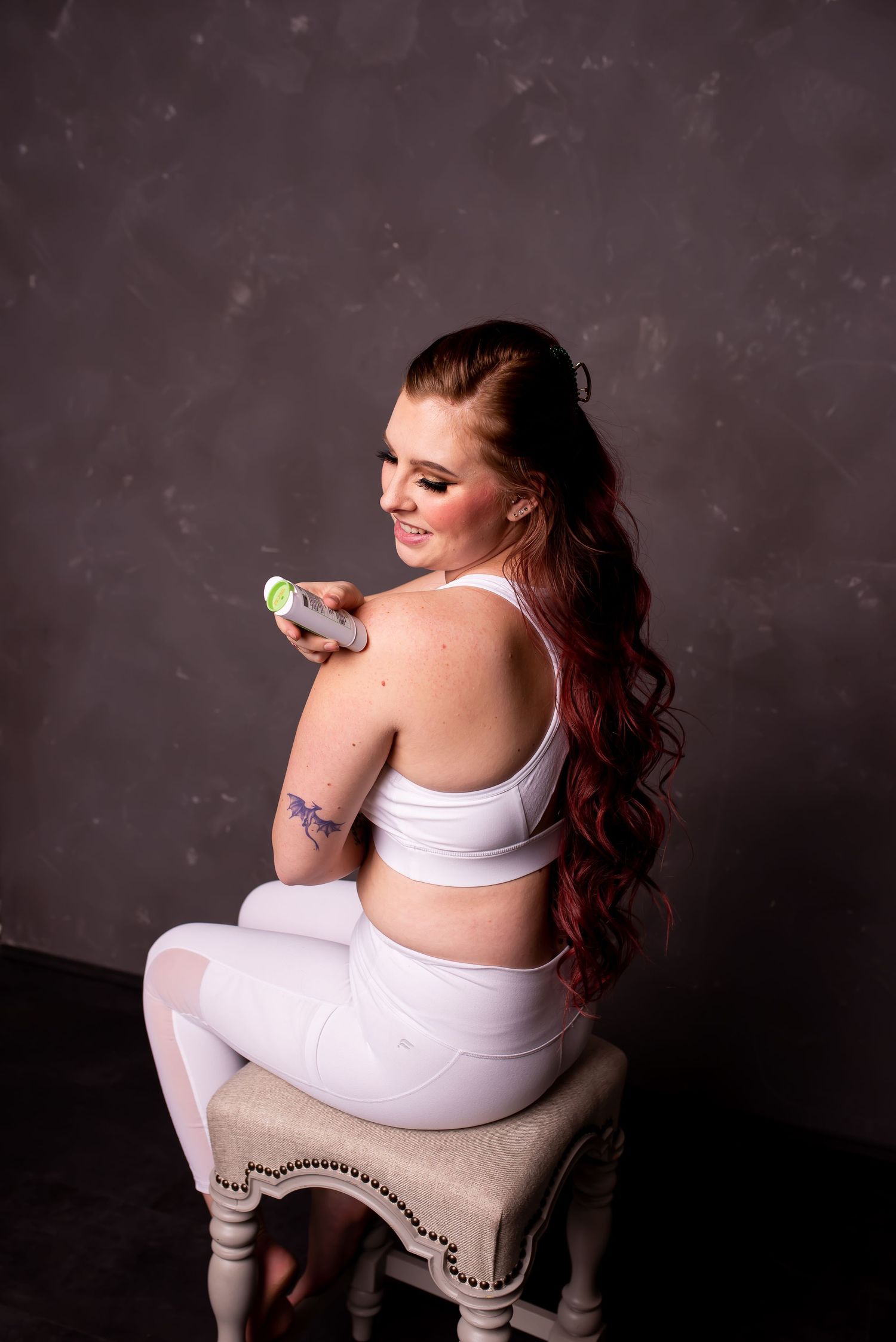 A woman in white athletic wear sits on a bench against a grey wall.