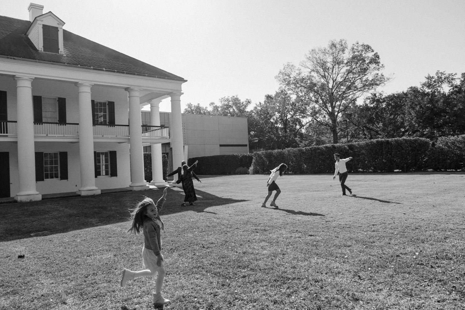 Children playing on the lawn of a white columned mansion in black and white.