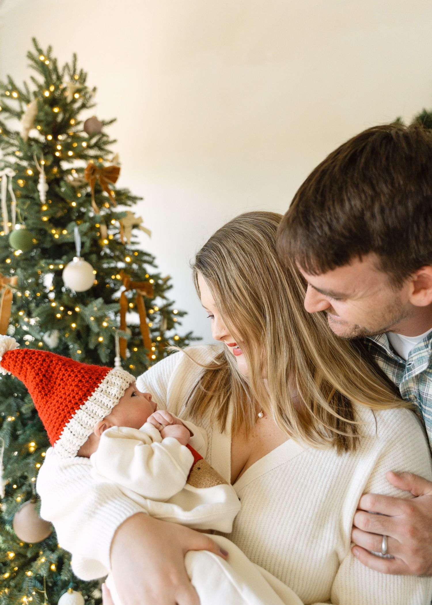 Mother in white dress holds young child near decorated Christmas tree in bright modern home.