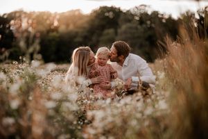 Mamma och pappa gosar med sin dotter bland vita blommor