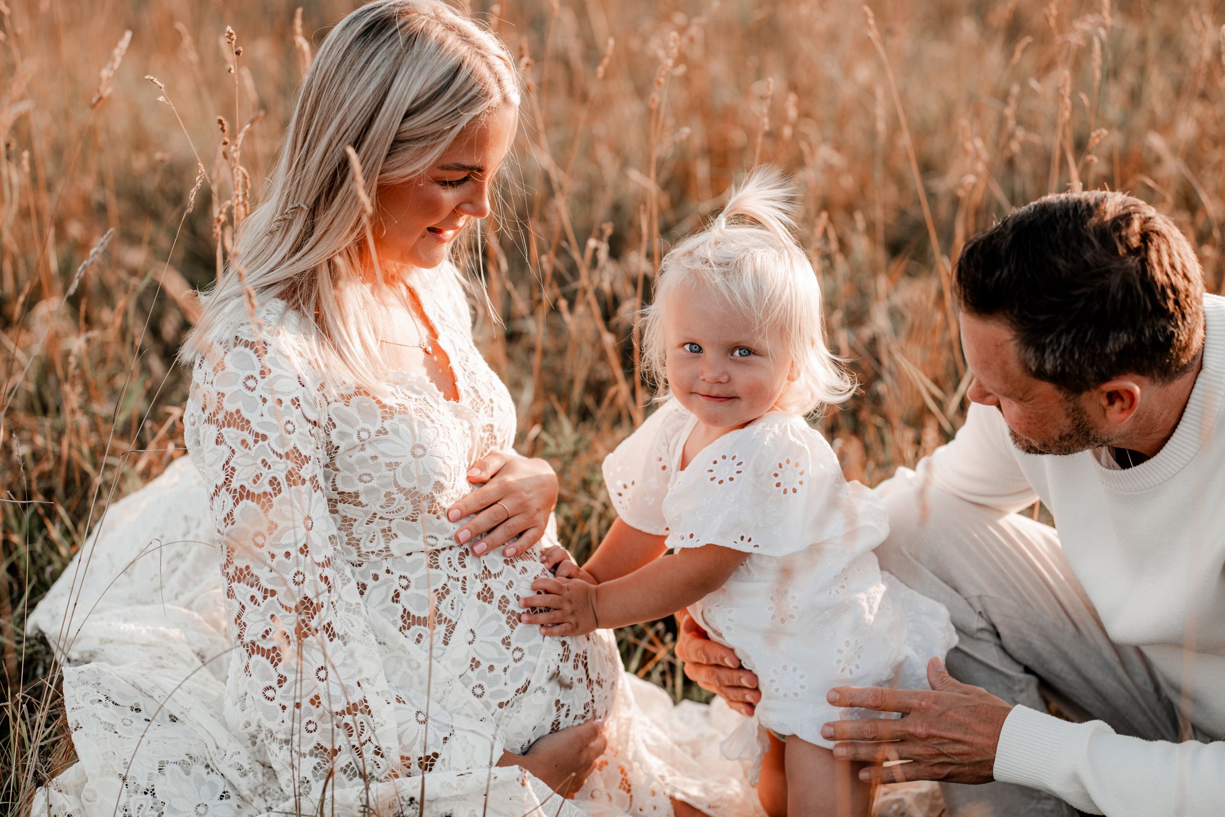 Familj på en äng i solnedgången väntar på lillasyster