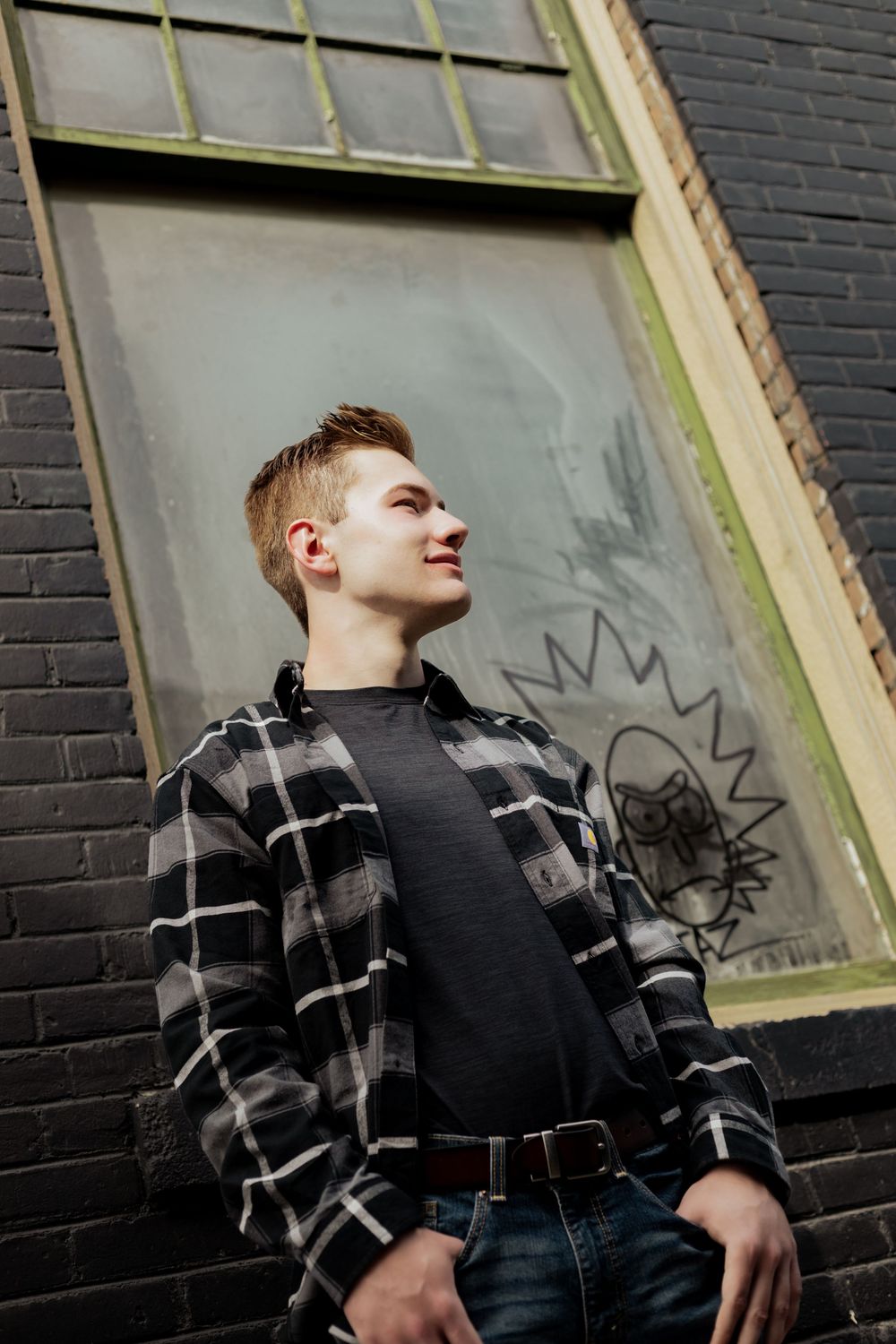 A person in a plaid shirt and dark vest stands against a black brick wall with graffiti in a multi-angle photo sequence.