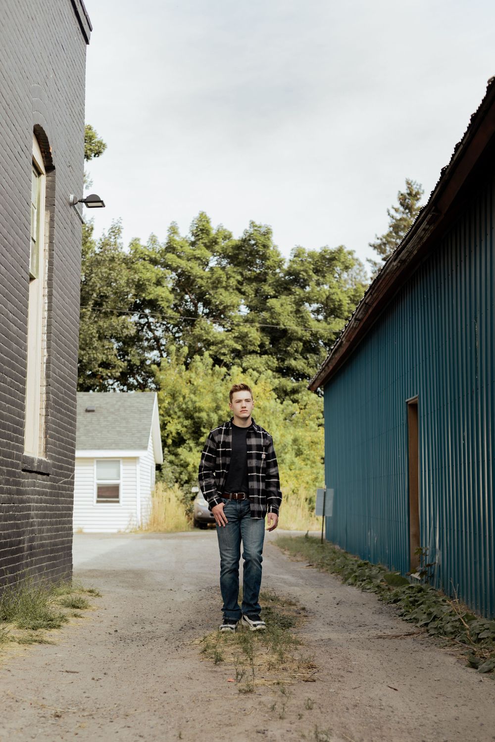 Person walking through a narrow alleyway between two buildings on an unpaved path lined with greenery.