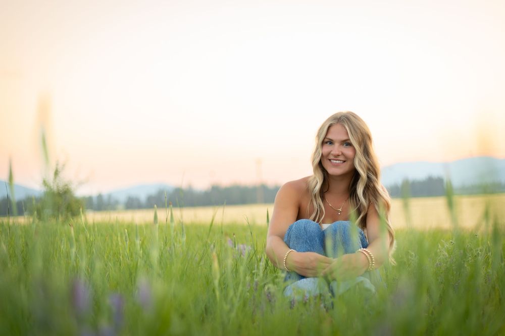 Woman in blue dress poses joyfully in a sunlit grassy meadow field during golden hour sunset.