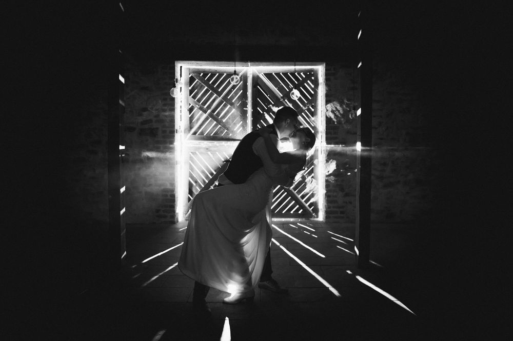 Black and white photo of a couple embracing silhouetted against a bright doorway in a dark barn.