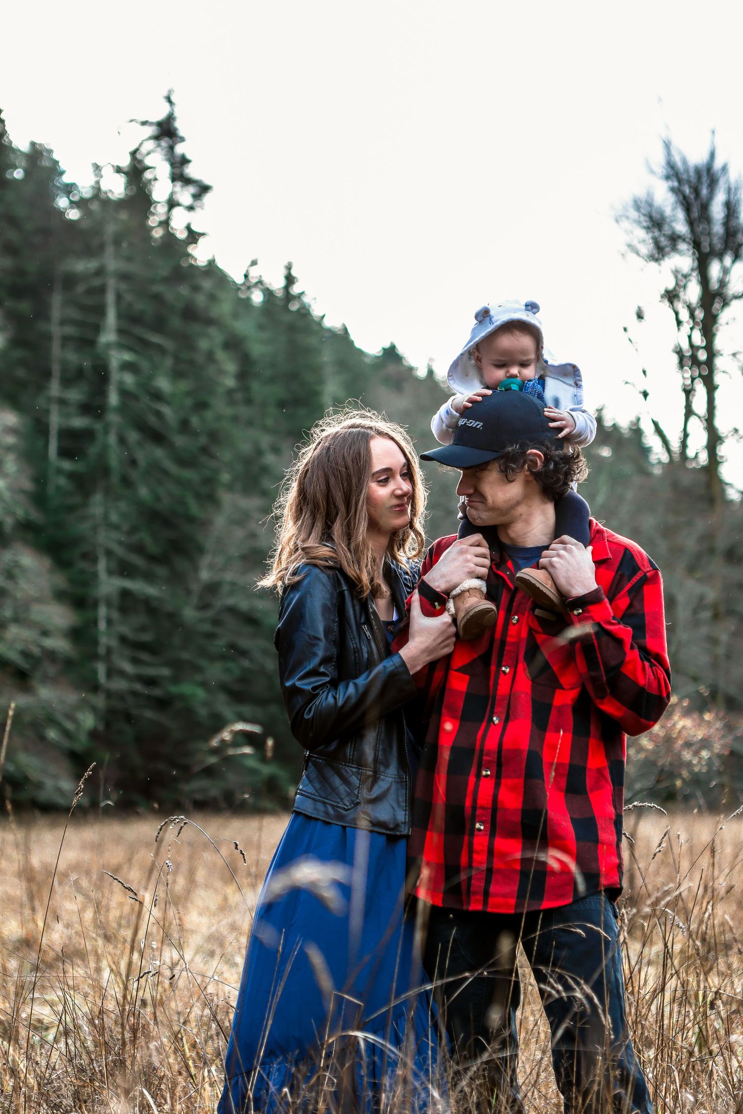 Family sharing a tender moment together in a rustic outdoor setting with evergreen trees.