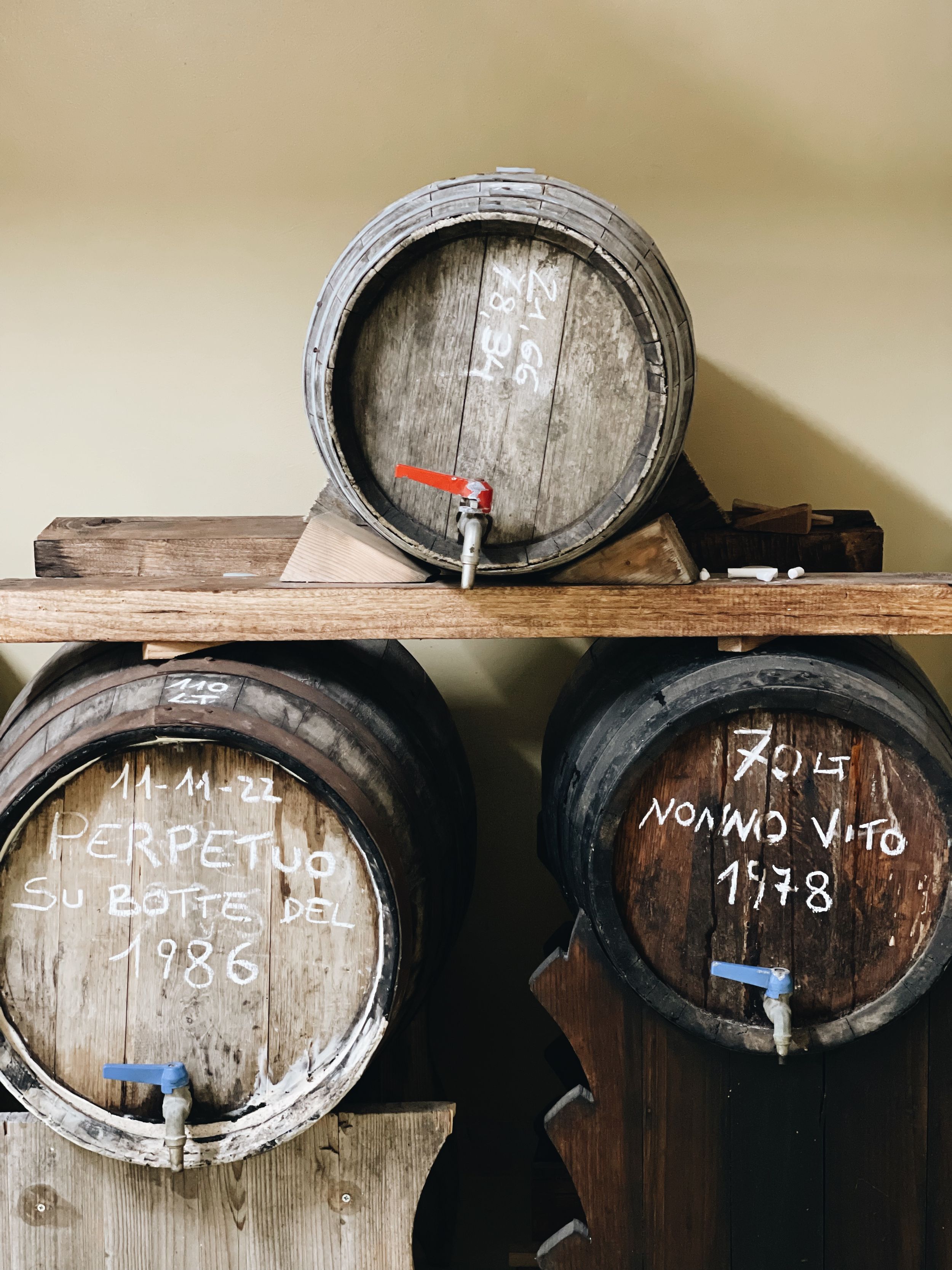 Old wooden wine barrels with chalk labels stored in a traditional cellar.