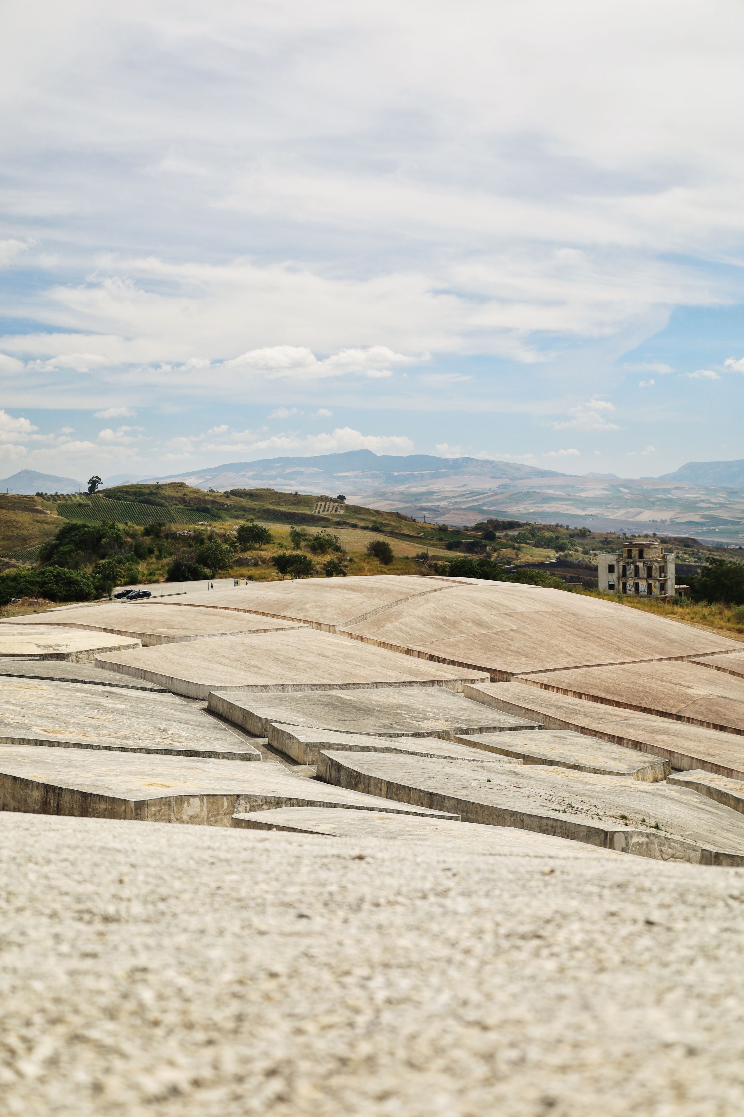 Terraced white limestone formations stretch across rolling hills with mountains visible in the distance under cloudy skies.