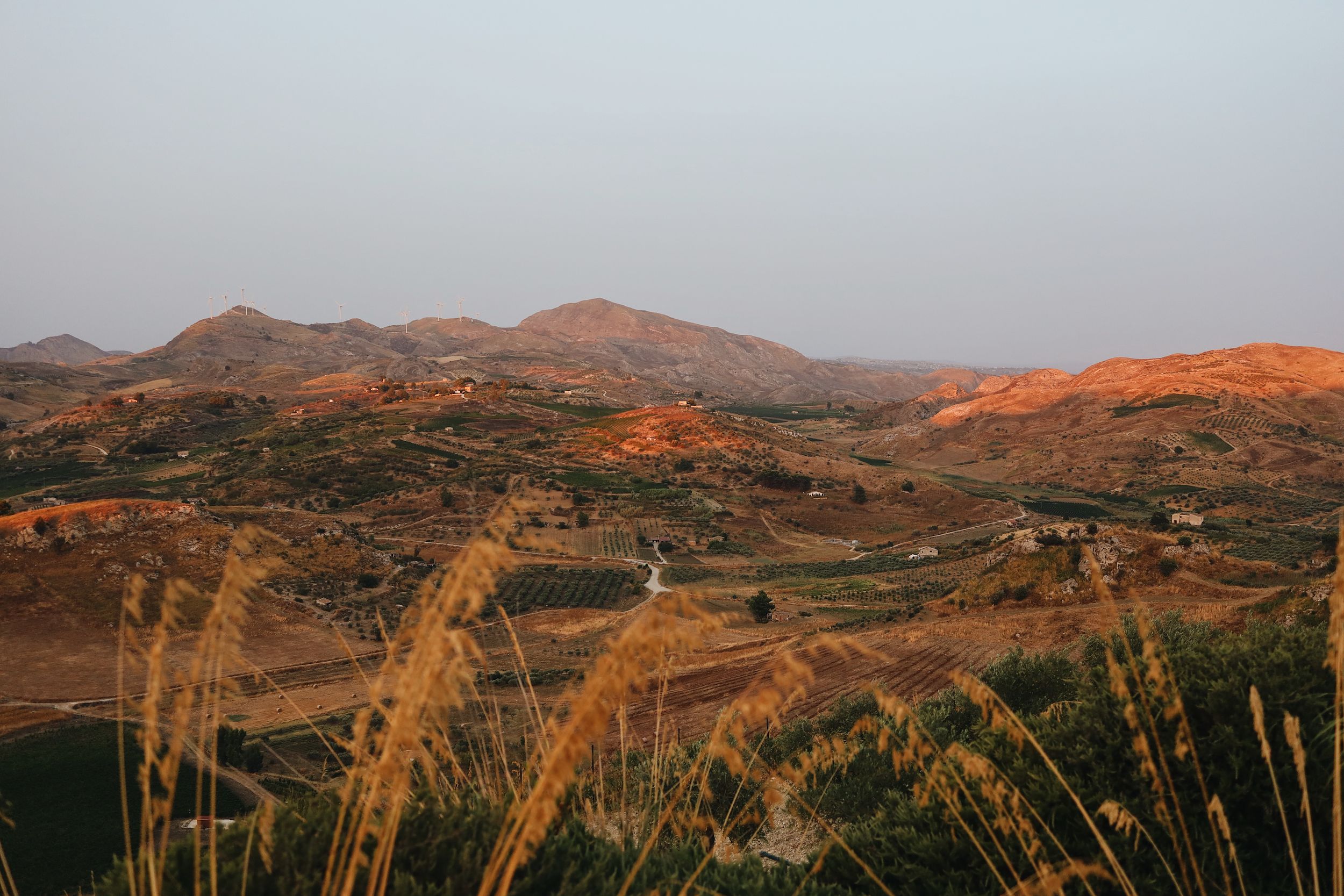 Rolling hills and mountains glow with golden light at sunset across a scenic California landscape.