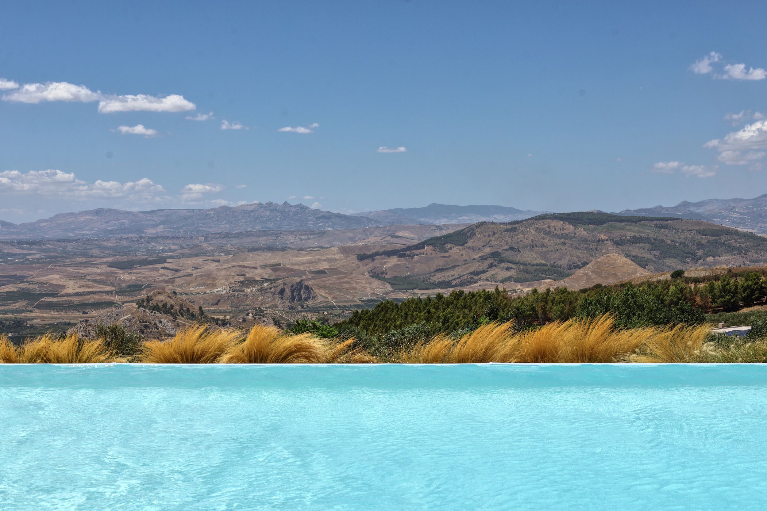 Panoramic mountain landscape with turquoise thermal pools cascading down white mineral terraces on a sunny day.