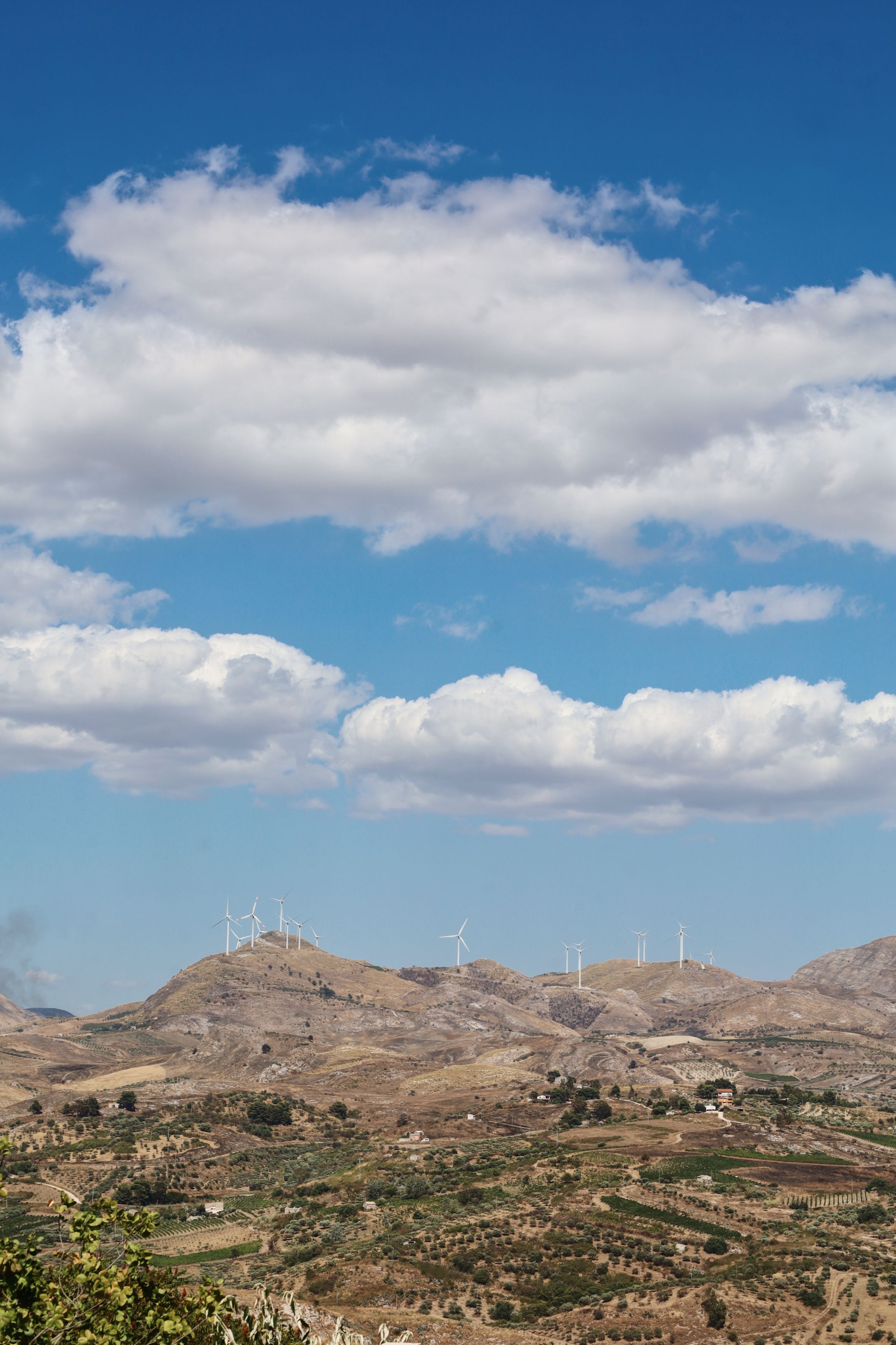 Panoramic view of mountainous landscape with wind turbines on distant ridges under blue sky.