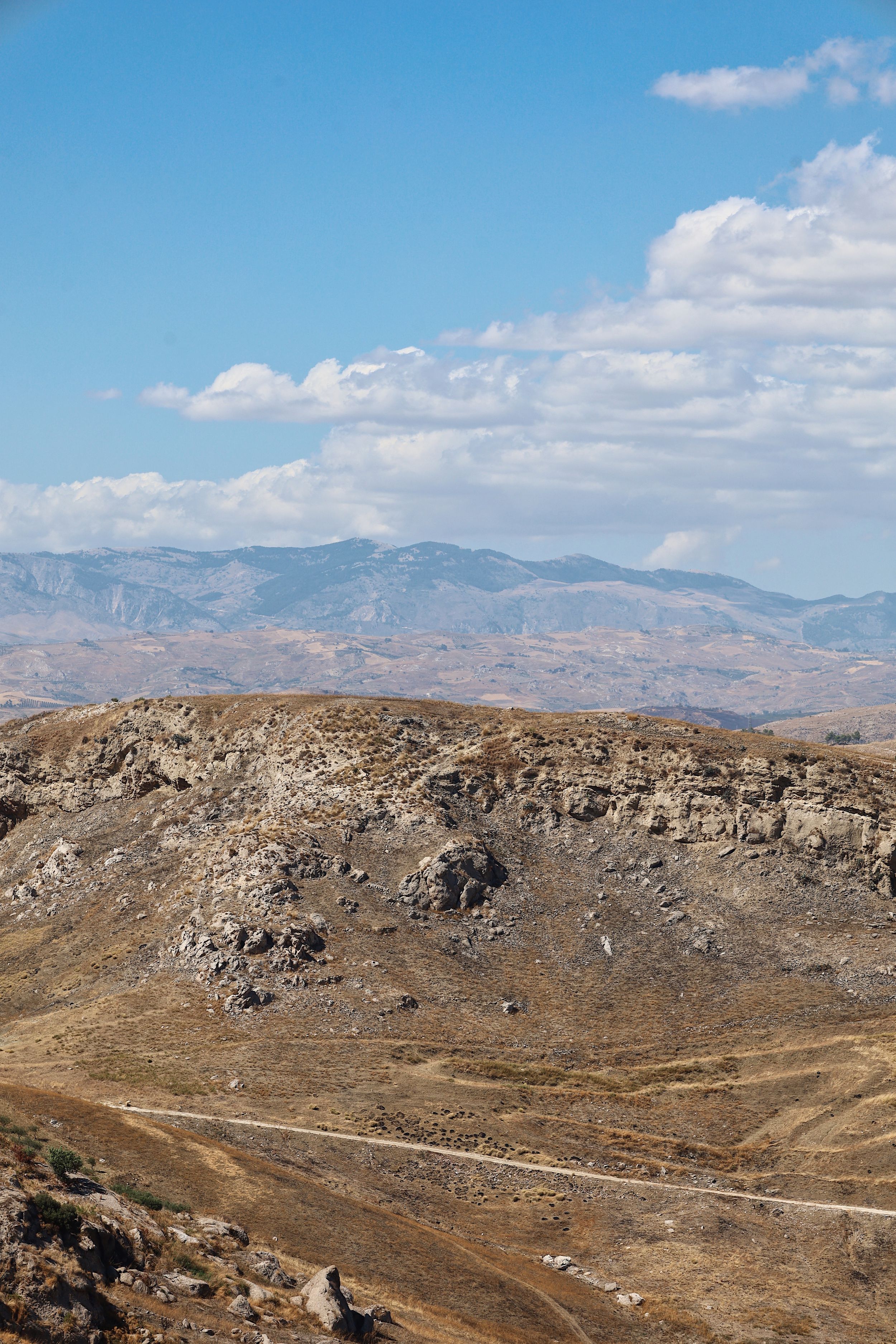 Rocky desert landscape with winding dirt road through rugged mountain terrain.