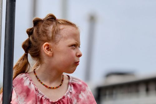 Child in pink dress looking to the side against light background.