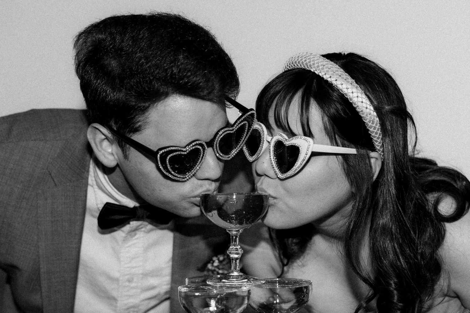 Fun photo of couple sharing a drink through heart-shaped sunglasses.