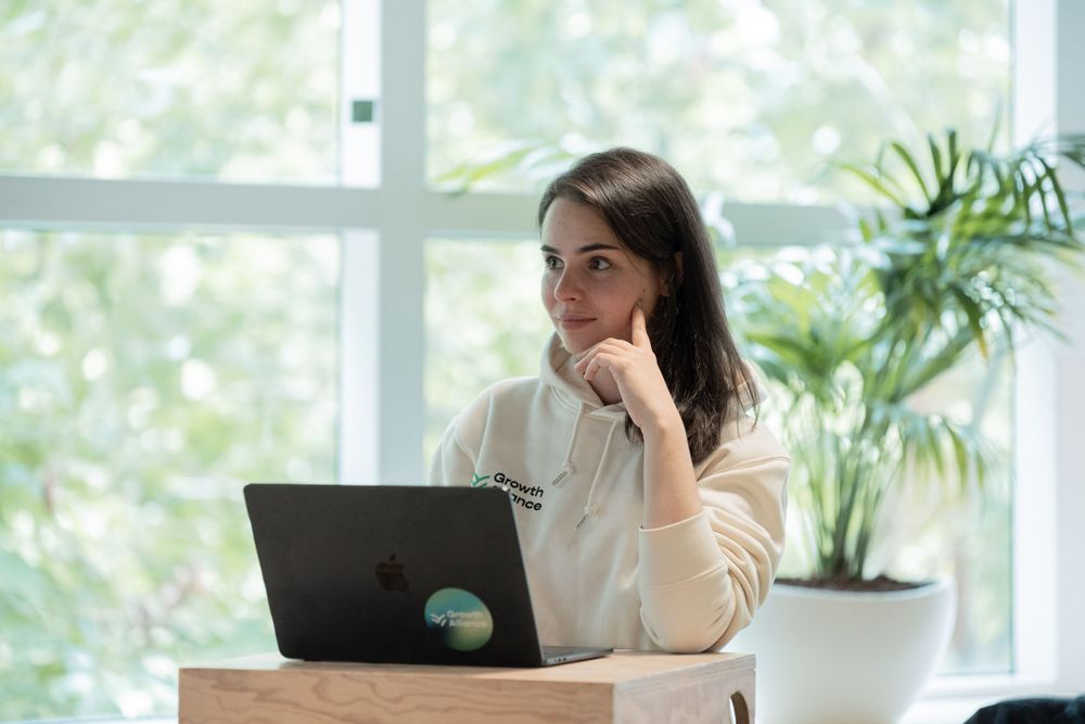 A person working on a laptop in a bright office space with plants and windows.