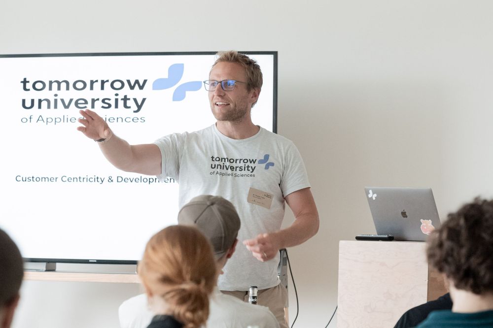 A speaker presenting in front of a screen displaying 'Tomorrow University' logo.