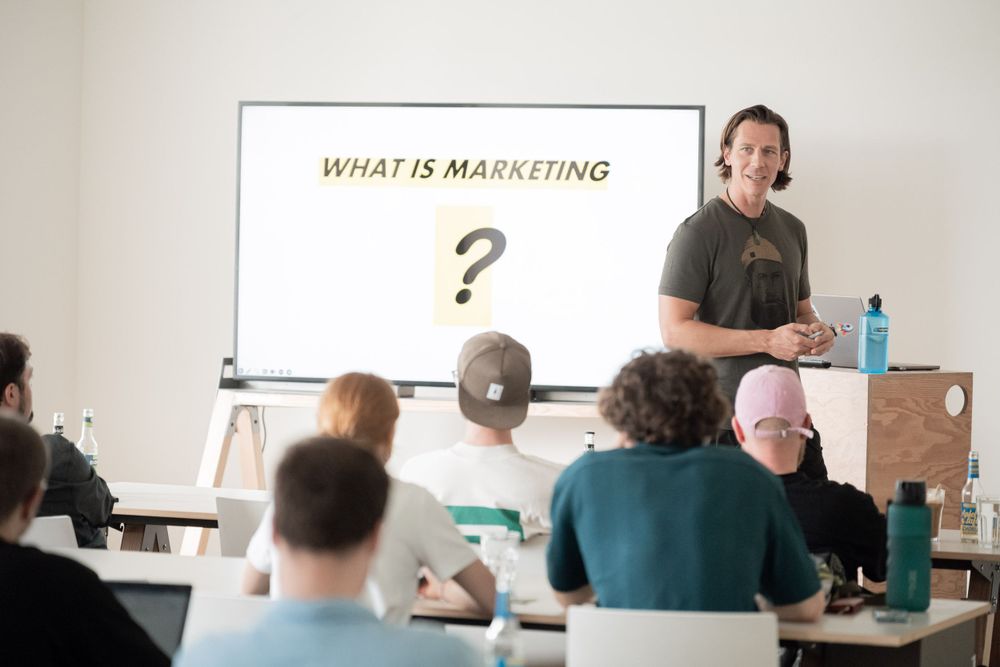 A classroom setting with a whiteboard displaying 'What is Marketing?' during a presentation.