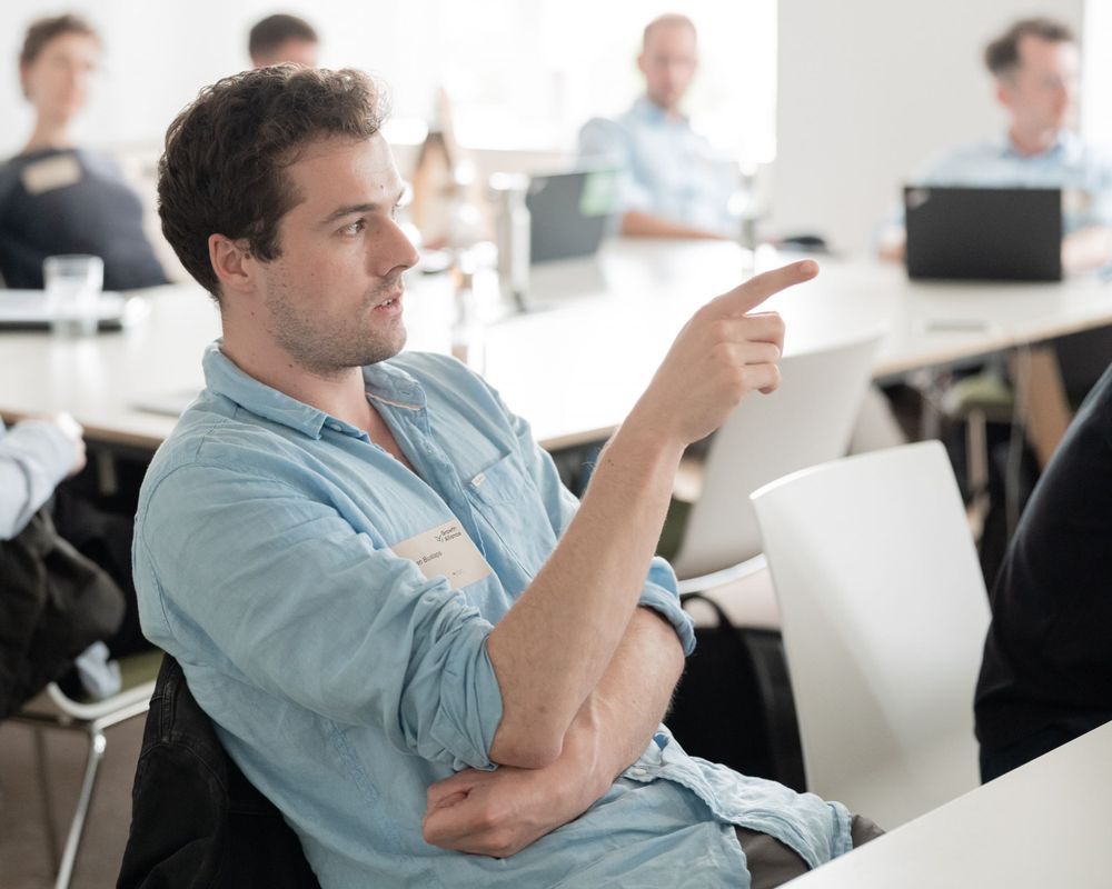 Person in casual attire gesturing during a meeting in a bright office space.