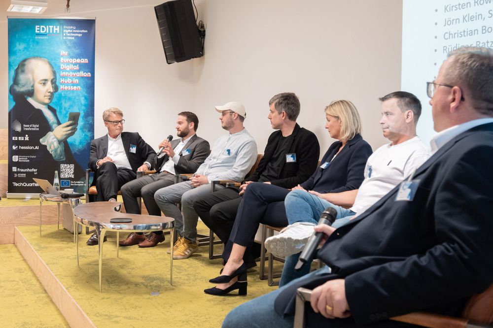 Panel discussion participants seated in chairs on stage at a business conference.