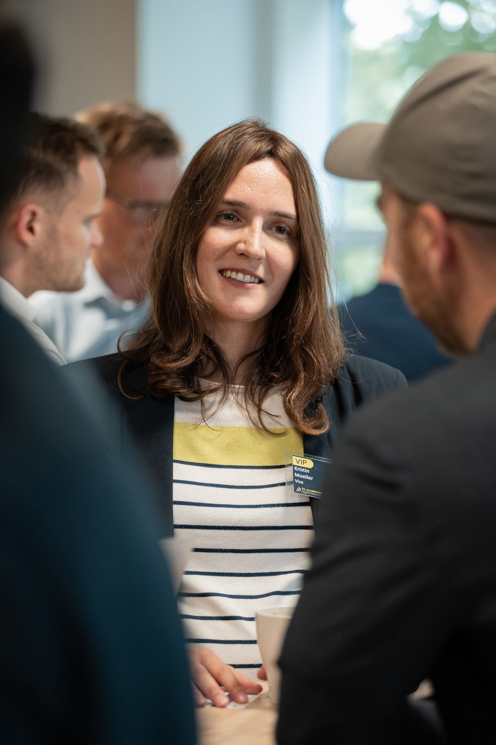 A person in a striped sweater smiling while networking with colleagues at an event.