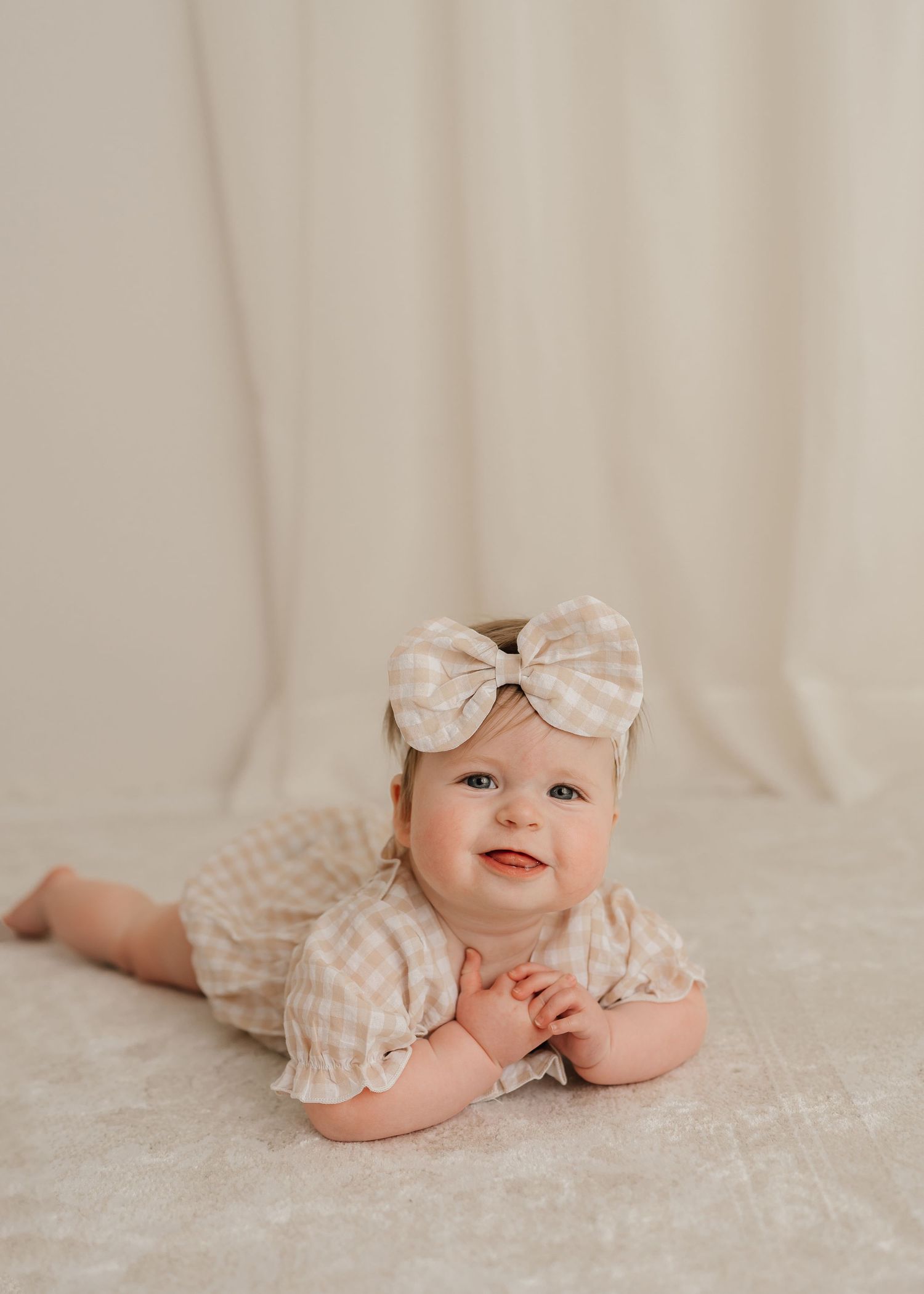 Baby in polka dot dress and bow headband lying on cream backdrop.